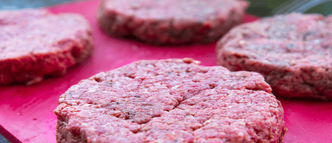 Close up view of burger patties on a red chopping board.