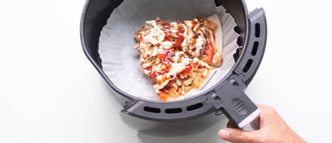 Someone using air fryer basket liners to help clean their air fryer