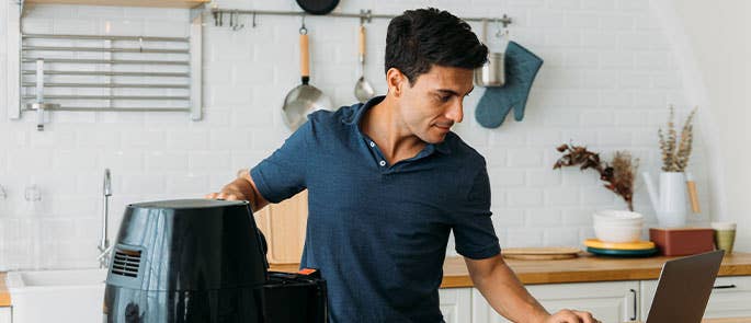 Person cleaning an air fryer and searching on laptop